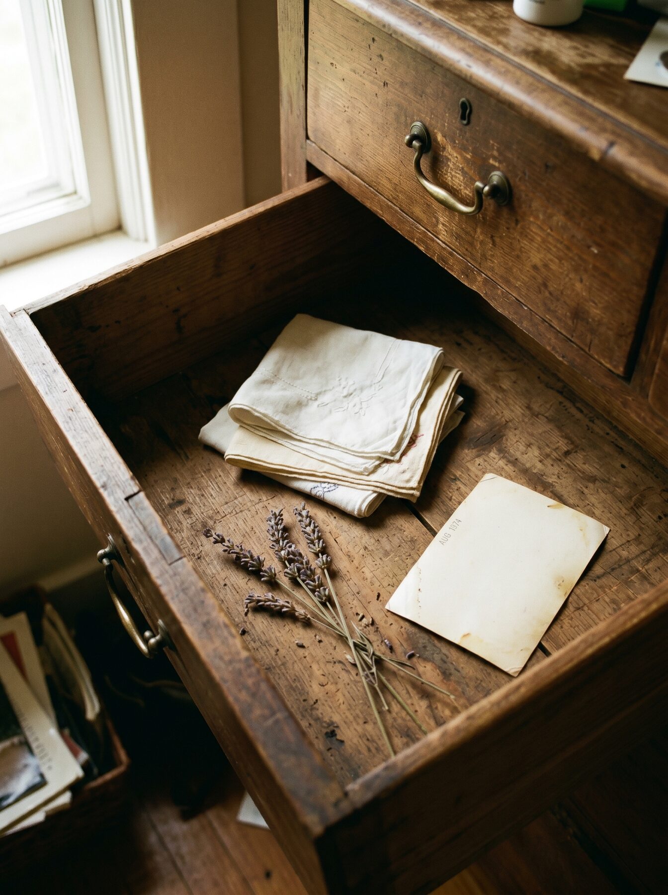 An open drawer of kept things: folded embroidered linen, dried lavender, and an old photograph dated August 1974.